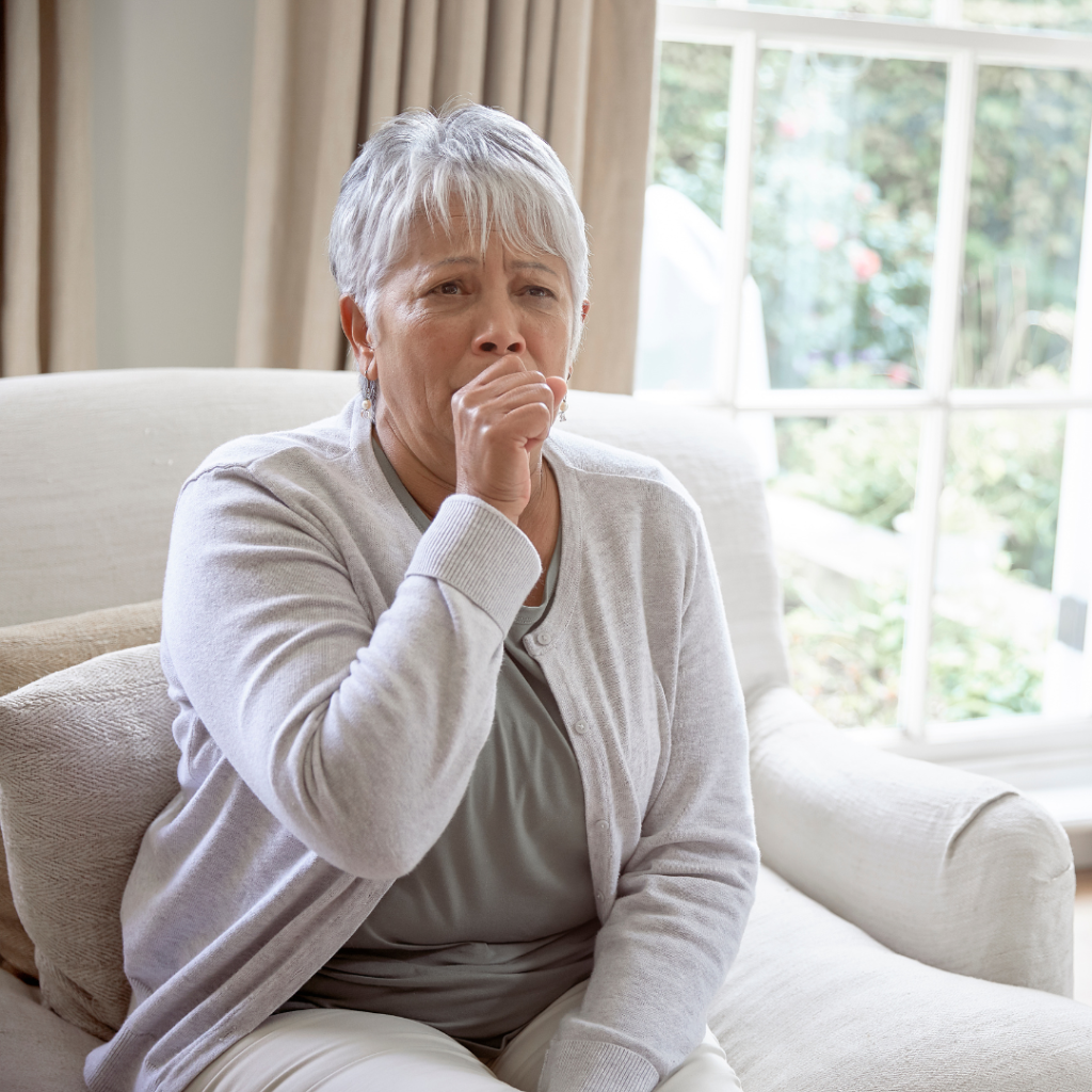 Senior Woman seated on couch coughing | Comfort Keepers Calgary | BLOG POST | Keeping Pneumonia Away from Your Aging Loved Ones