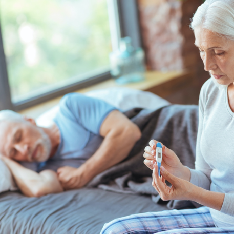 Senior man sleeping on bed next to seated senior woman | Comfort Keepers Calgary | Preventing and Treating Pneumonia in Seniors | BLOG POST