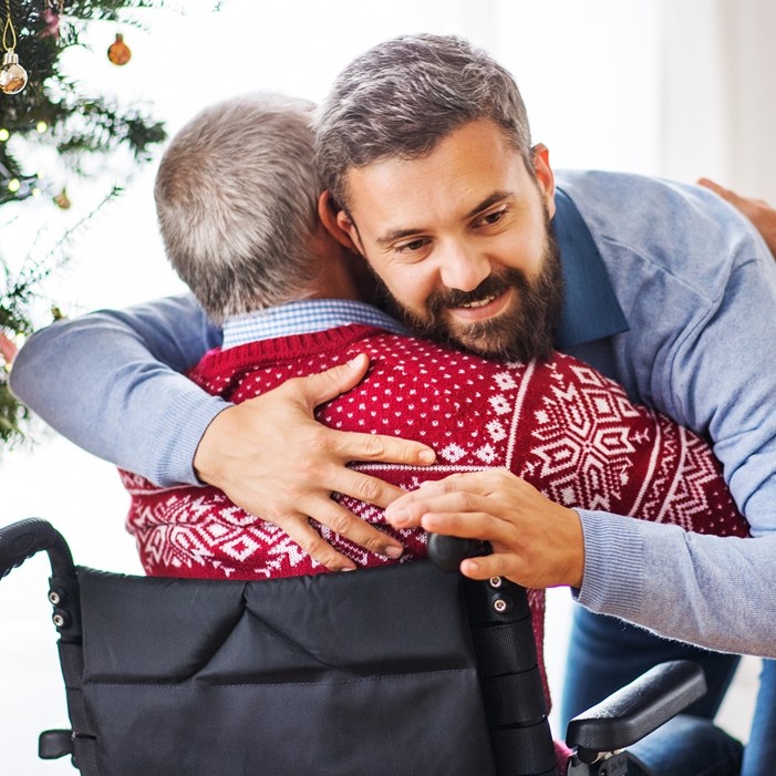 Individual male hugging a senior male who is sitting in a wheelchair | Comfort Keepers Calgary | BLOG POST | Respite Care for Your Loved One