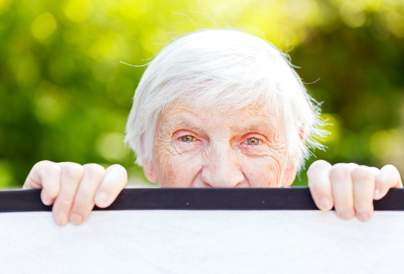 Senior woman peeking over fence | Comfort Keepers Calgary | BLOG POST | Coping with Sundown Syndrome