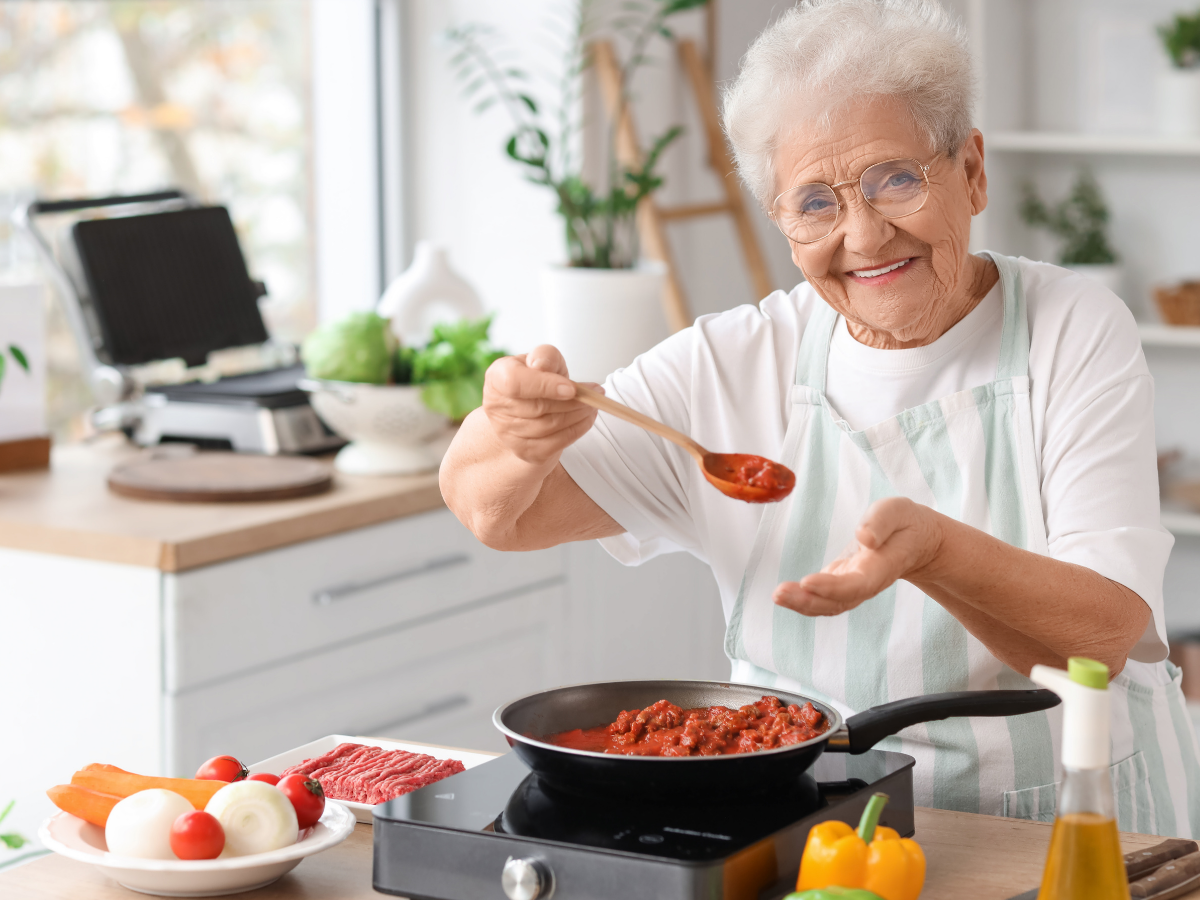 A senior woman cooking in her kitchen | The Relationship Between Diet and Fatigue for Edmonton's Seniors | Comfort Keepers Edmonton