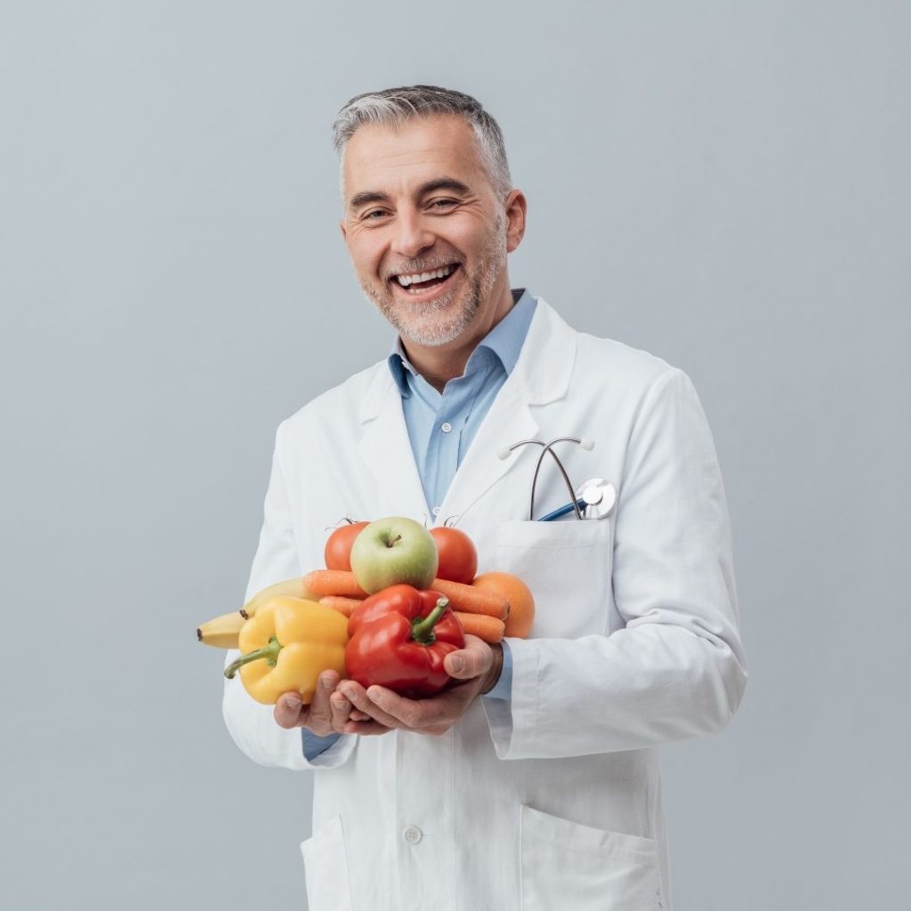 Man in white Doctor's coat holding two handfuls of fruits and veggies 