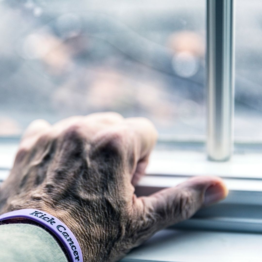 A Senior's hand grip the window sill wearing a "Kick Cancer" bracelet