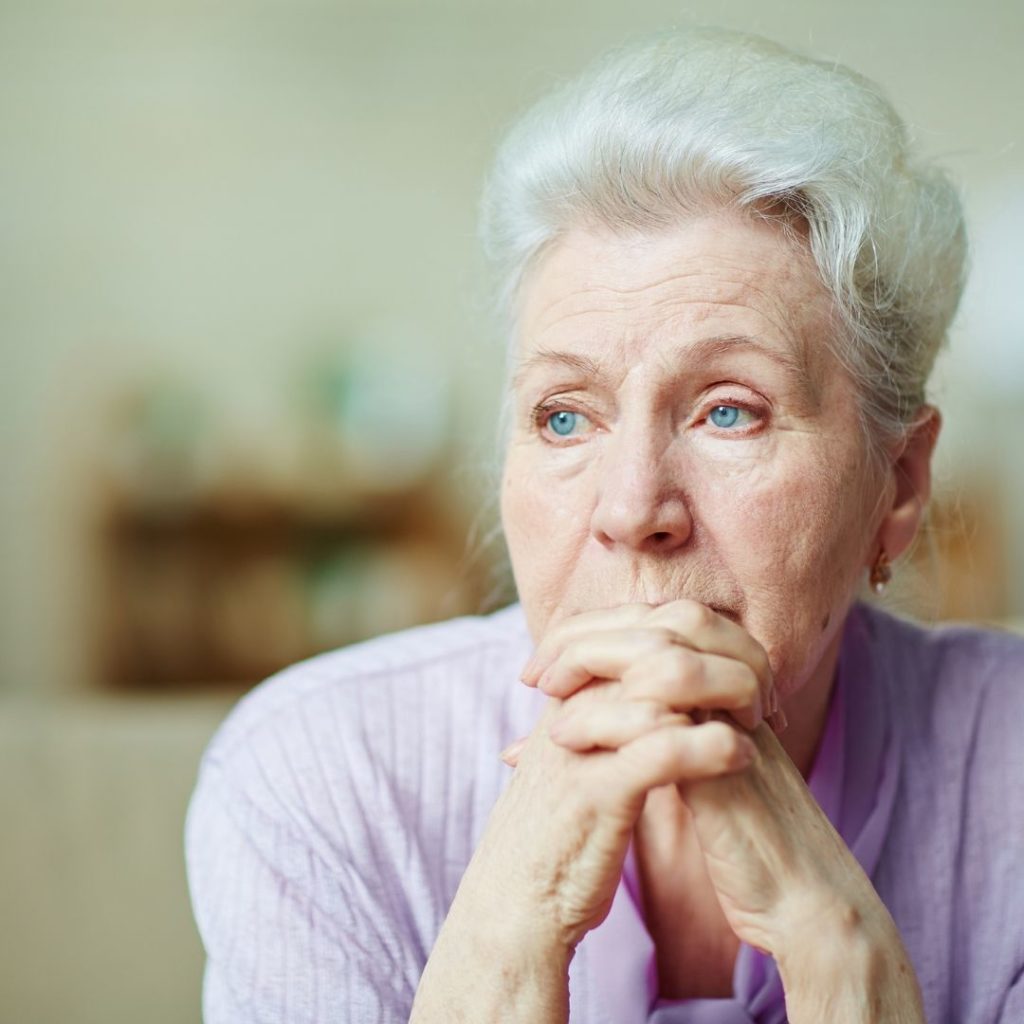 Photo of elderly woman looking off into the distance with fingers interlaced