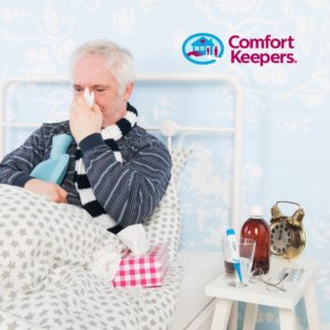 Senior Male in bed sick with night table featuring medicine. Comfort Keepers logo.