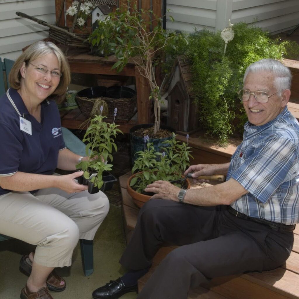 Caregiver and senior enjoying gardening together in a yard.