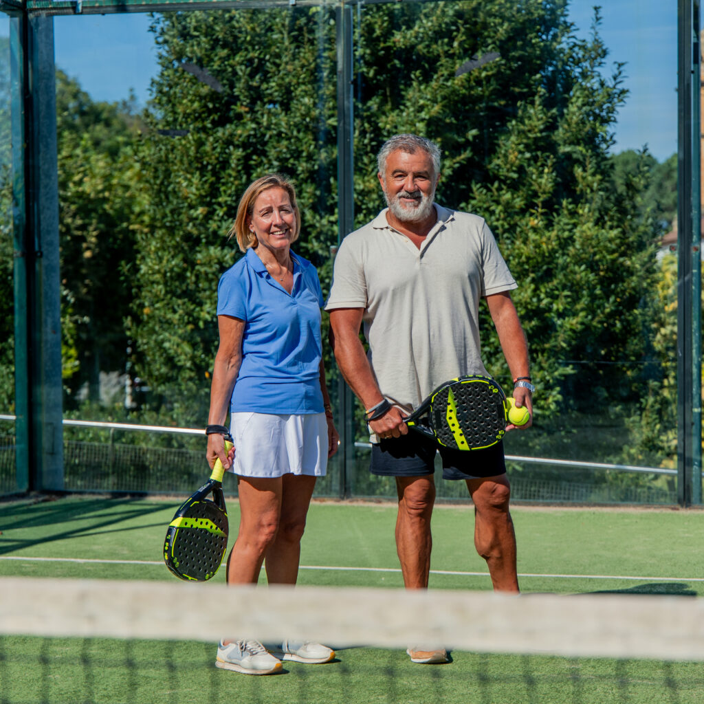An older man and woman pose on a pickleball court, demonstrating how the game improves social connection and physical health.