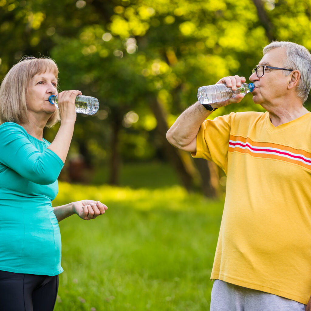 Older man and woman staying hydrated outdoors with bottled water – in home senior care Guelph