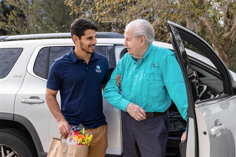 Comfort Keeper in home caregiver assisting senior with exiting the car.