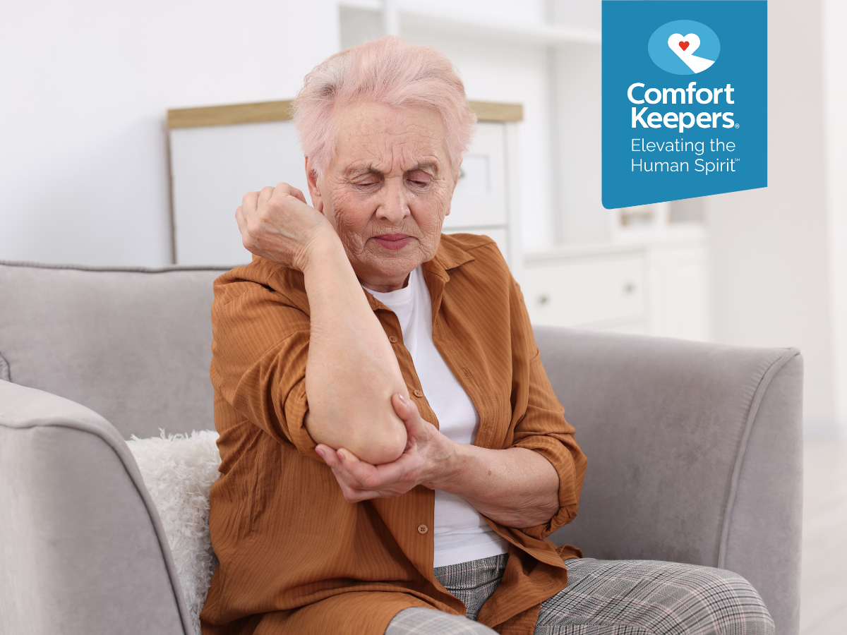 A senior woman seated on a couch holding her elbow | Promoting Bone Health | Comfort Keepers North and West Vancouver