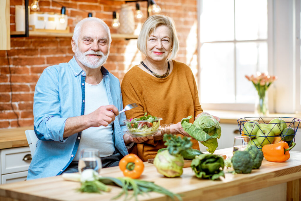 Older man and woman smiling while making a nutritious meal with fresh vegetables – in home senior care Ottawa & Kanata