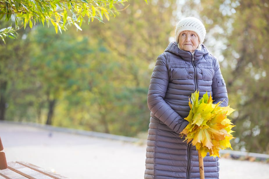 older woman standing alone outdoors in the park during the fall season.