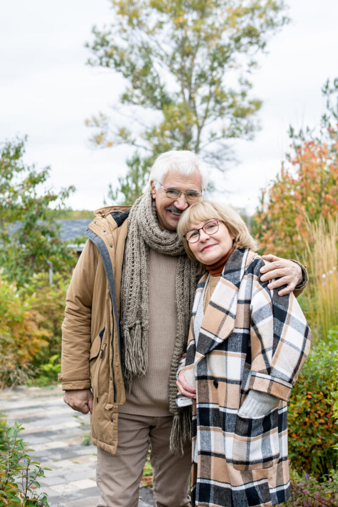 older couple standing closely together outdoors, during the fall season