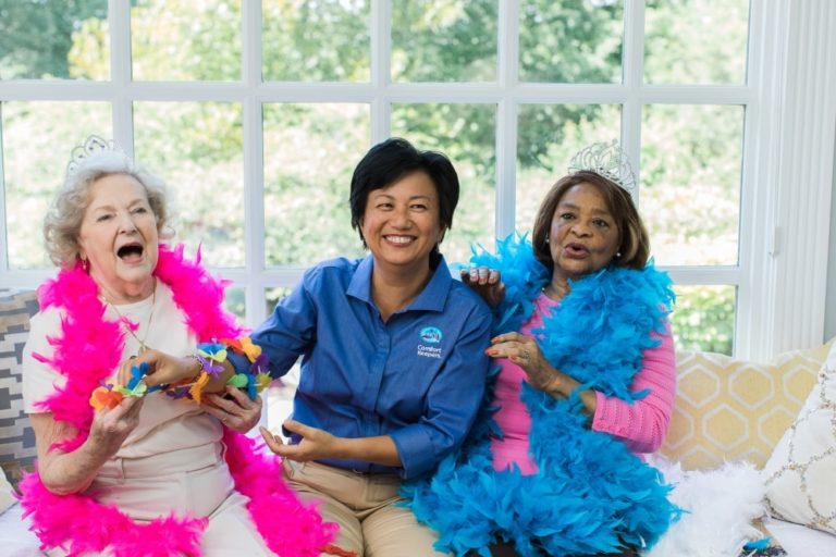 A two elderly woman having fun with Comfort Keepers caregiver that sits between them.