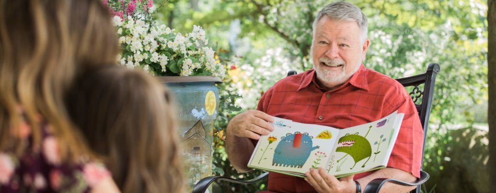 An old man, having a great time with his grandchild reading an animal book.