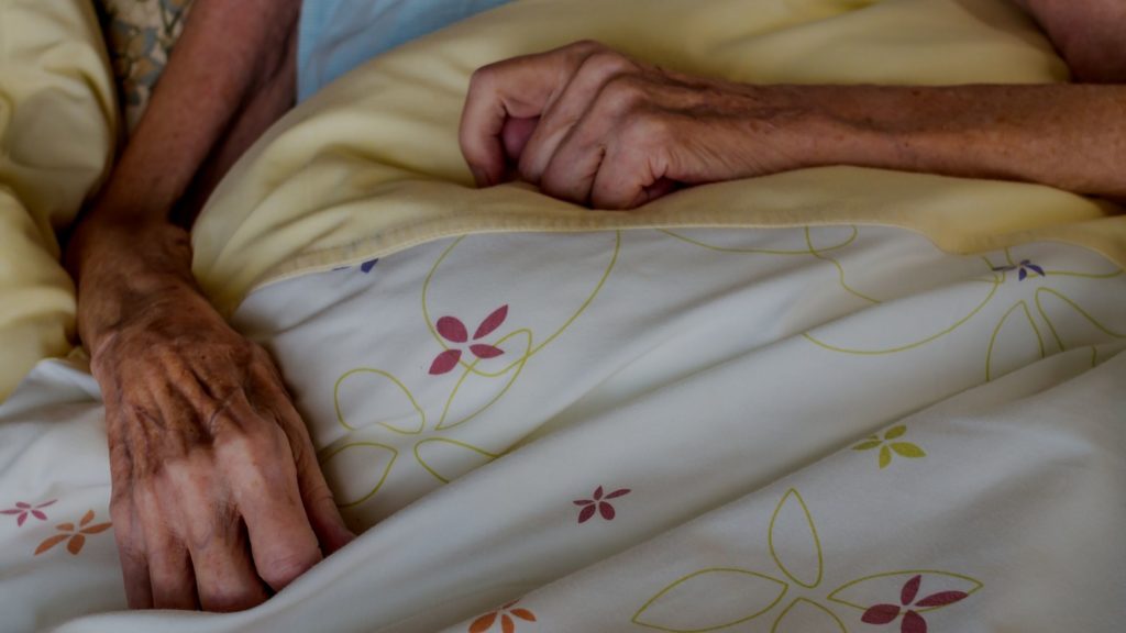 elderly woman's hands resting on top of a bedsheet