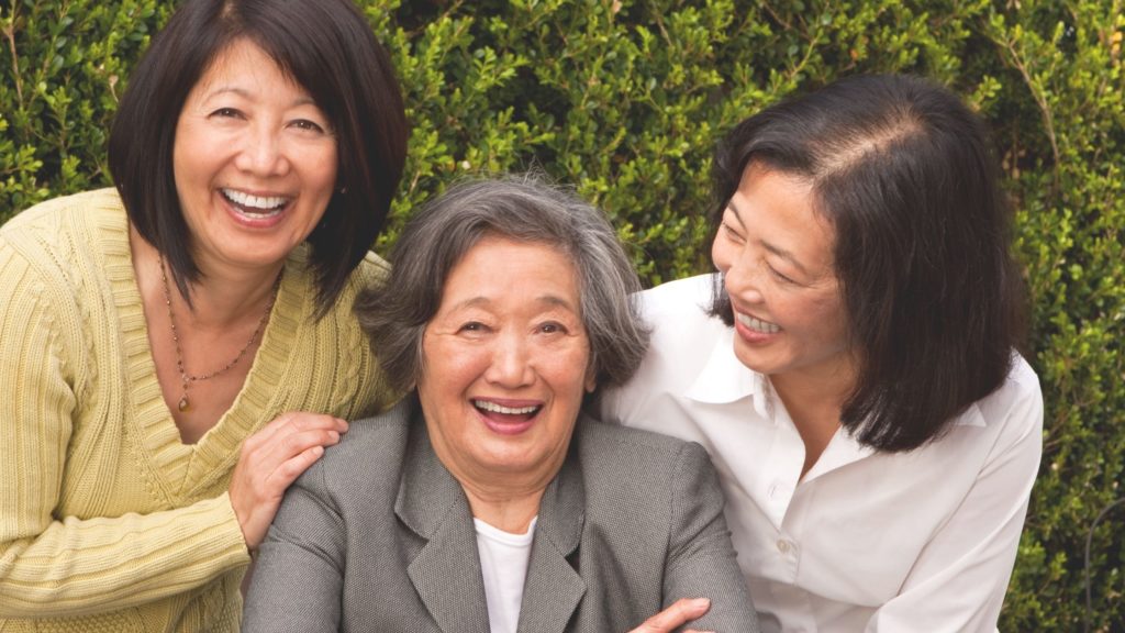 Two adult woman leaning on their senior mother smiling