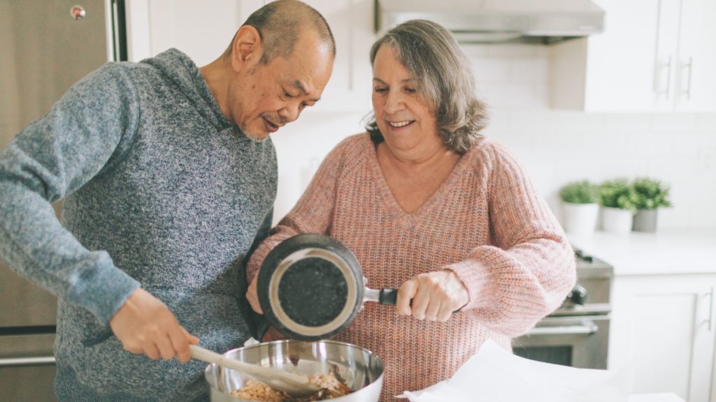 A senior man and woman in the kitchen cooking a meal together. 
