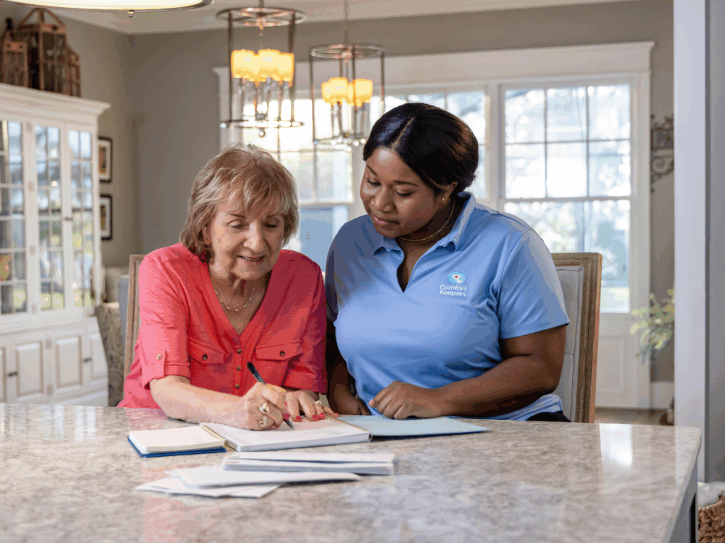 Senior woman seated at counter with caregiver going over paperwork | A Family Guide to In-Home Care Needs Assessment & Personalized Planning | Comfort Keepers Ridge Meadows | BLOG POST