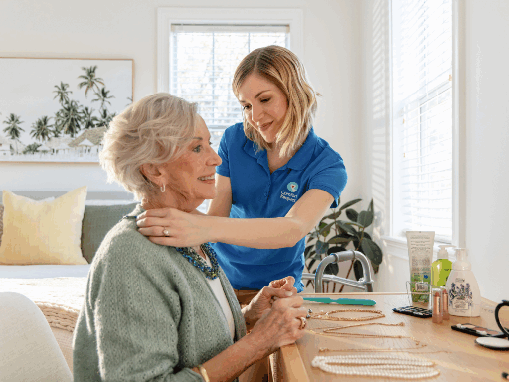 Senior woman seated at dressing table with caregiver fixing a necklace in place | That Gut Feeling: 7 Subtle Signs Your Elderly Parent Might Need More Help at Home | Comfort Keepers Tri-Cities | BLOG POST