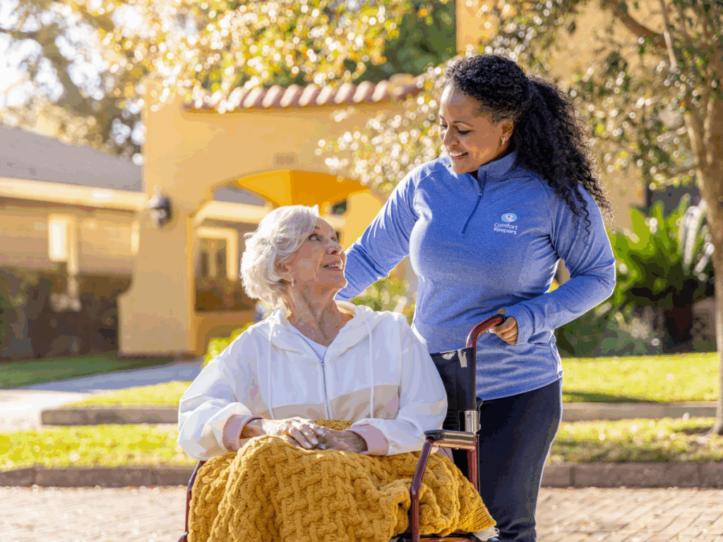 Senior woman seated in wheelchair with caregiver | The Benefits of At-Home Dementia Care: A Comparative Guide for Tri-Cities Families | Comfort Keepers Tri-Cities | BLOG POST