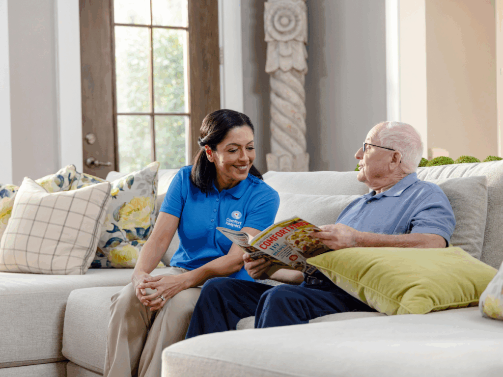 Senior male seated on couch with caregiver | Living Alone Without Friends and Family | Comfort Keepers Tri-Cities | BLOG POST