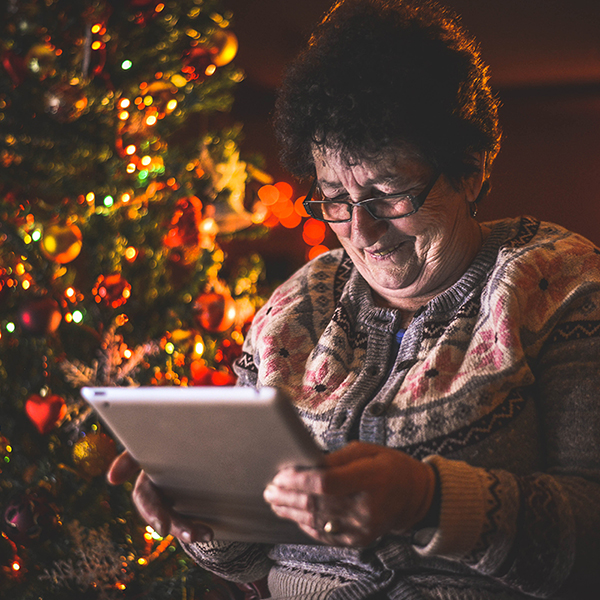 Senior woman looking at device in front of Christmas tree | Bring Seniors Comfort and Joy | BLOG POST | Comfort Keepers Vancouver