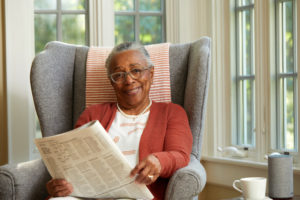 Senior woman seated in armchair reading paper and smiling | Wellness During Self-Isolation | BLOG POST | Comfort Keepers Vancouver