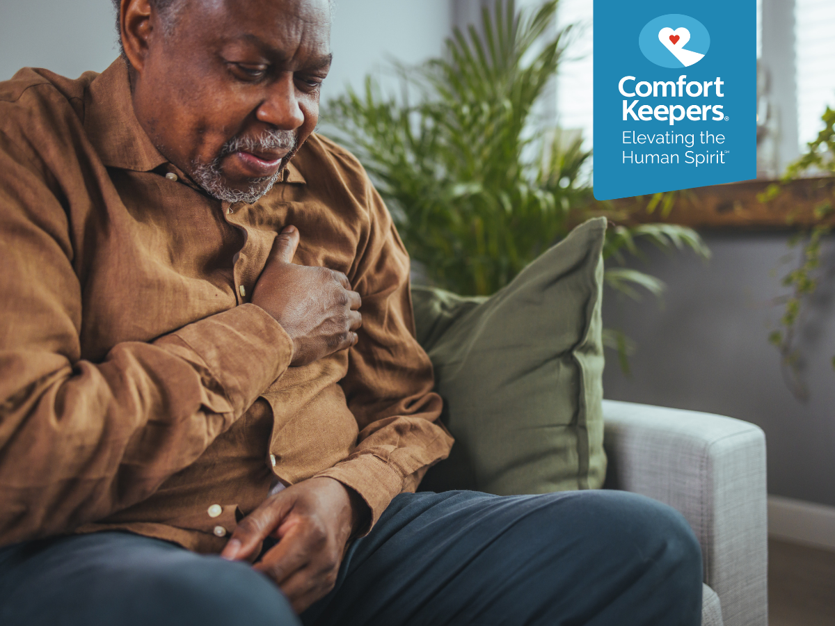 A senior man sitting on his couch clutches his chest | What Does a Heart Attack Look Like? | Comfort Keepers Victoria