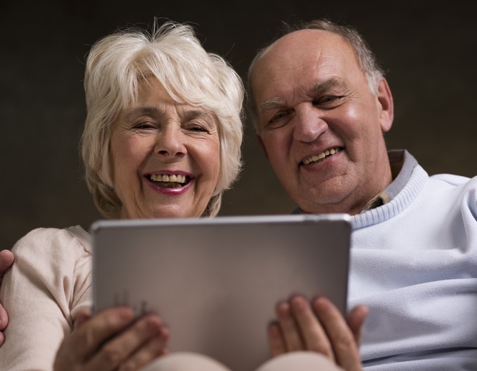 Seniors smiling at technical device, presumably connected | Staying Positive | BLOG POST | Comfort Keepers Victoria